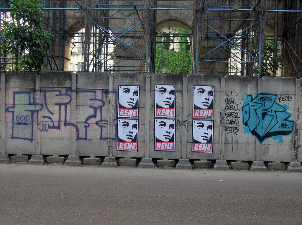 Wheat-pasted campaign posters on concrete barriers with graffiti, urban street.