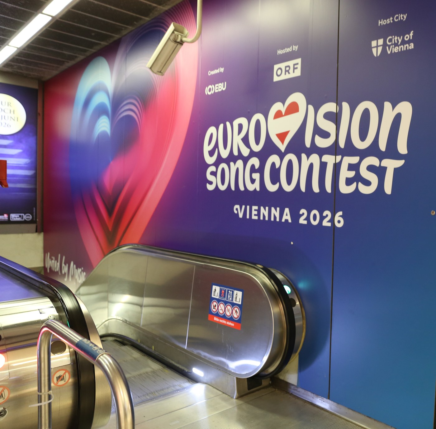 Large campaign poster wrap covering a metro station wall next to an escalator.